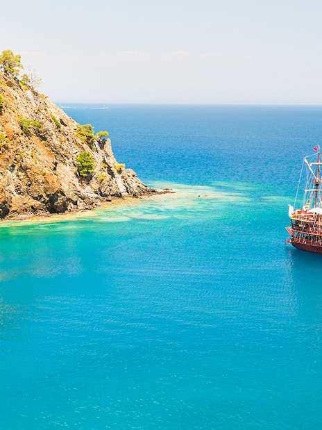 Boat sailing near rocky coastline in Phaselis during a guided tour from Antalya.