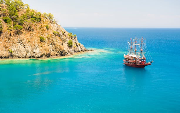 Boat sailing near rocky coastline in Phaselis during a guided tour from Antalya.
