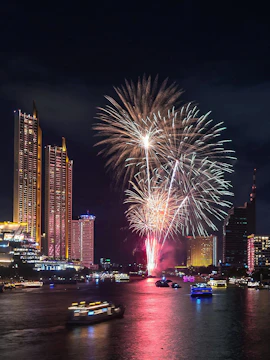 Fireworks over Bangkok skyline at night, reflecting on the river during New Year celebration.