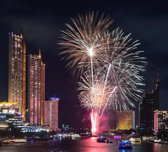 Fireworks over Bangkok skyline at night, reflecting on the river during New Year celebration.