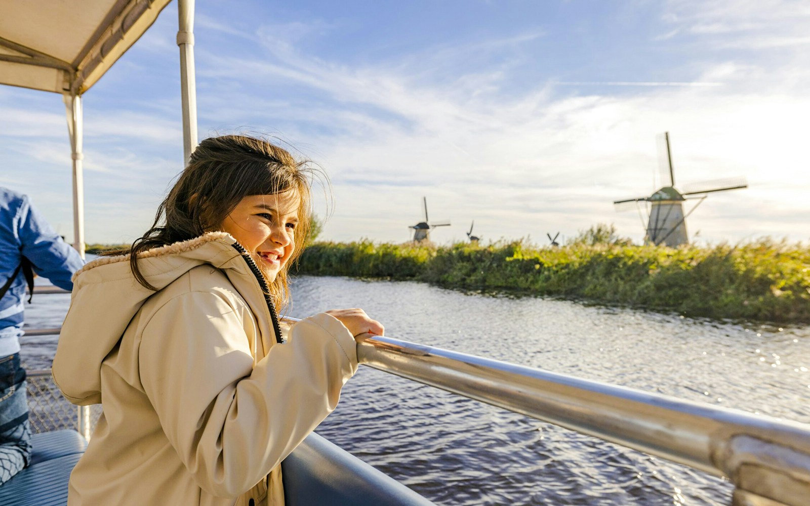 Child enjoying a boat tour with windmills at Kinderdijk in the background.