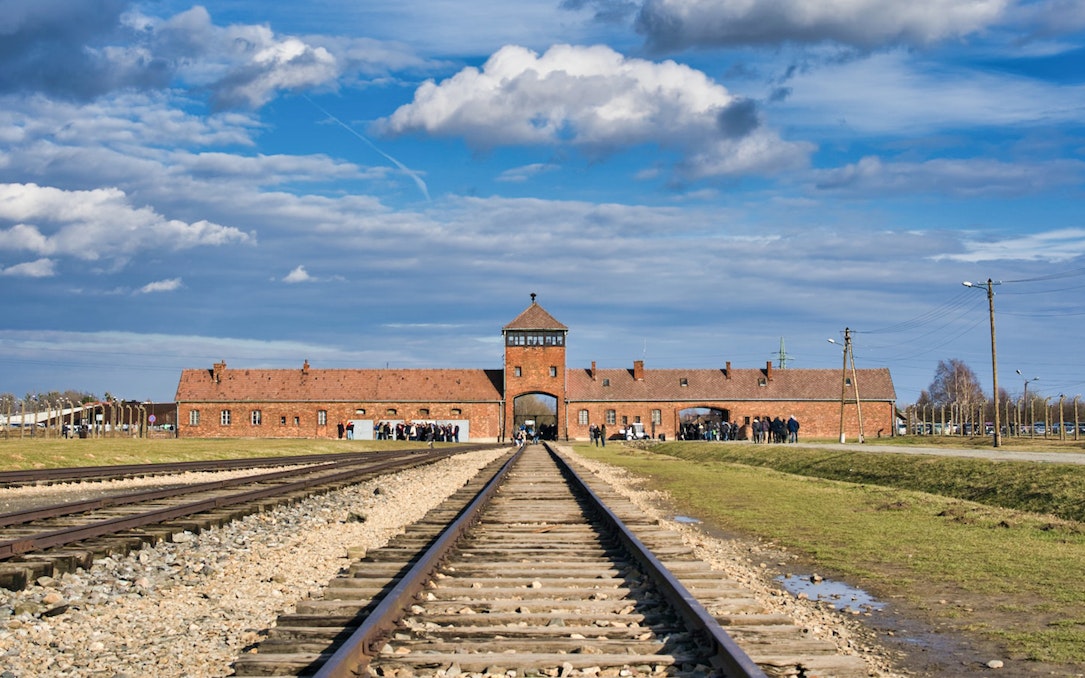 Railway tracks leading to Auschwitz concentration camp entrance under a cloudy sky.