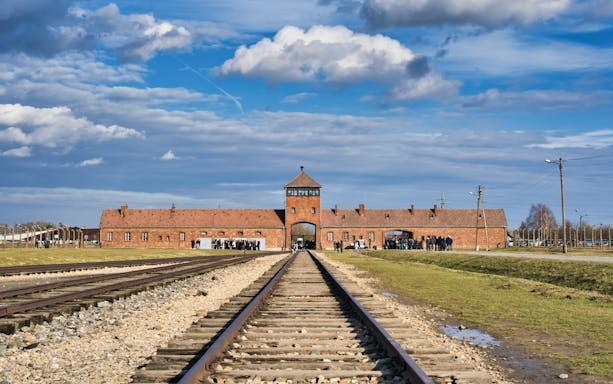 Railway tracks leading to Auschwitz concentration camp entrance under a cloudy sky.