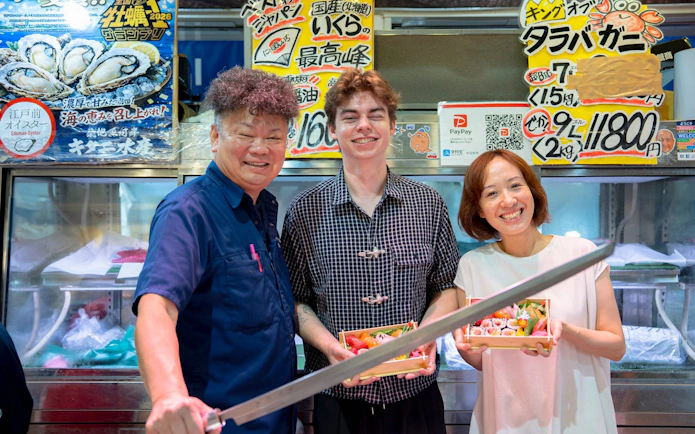 Visitors holding sushi bento boxes at Tsukiji Market during a tuna tasting tour.