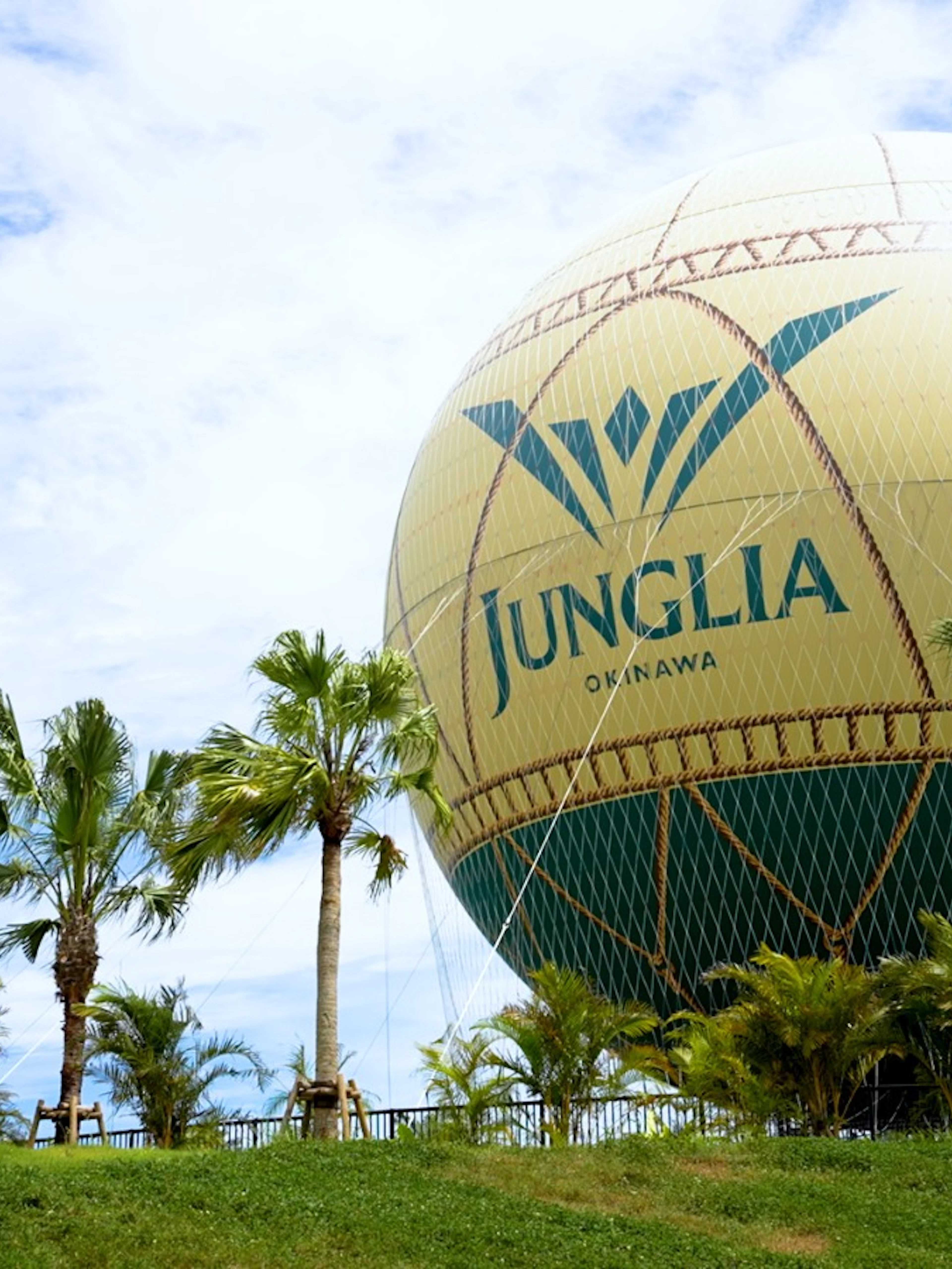 Hot air balloon at JUNGLIA OKINAWA Park surrounded by palm trees.