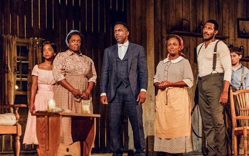 Cast of "Purlie Victorious" on stage in period costumes, standing in a rustic setting.