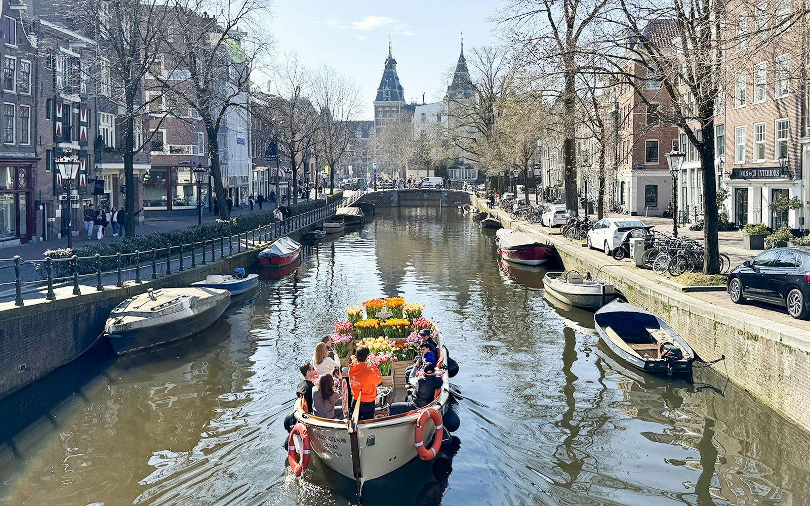 Boat sailing through Amsterdam canal during Tulip Tour, showcasing vibrant tulip fields and historic cityscape.