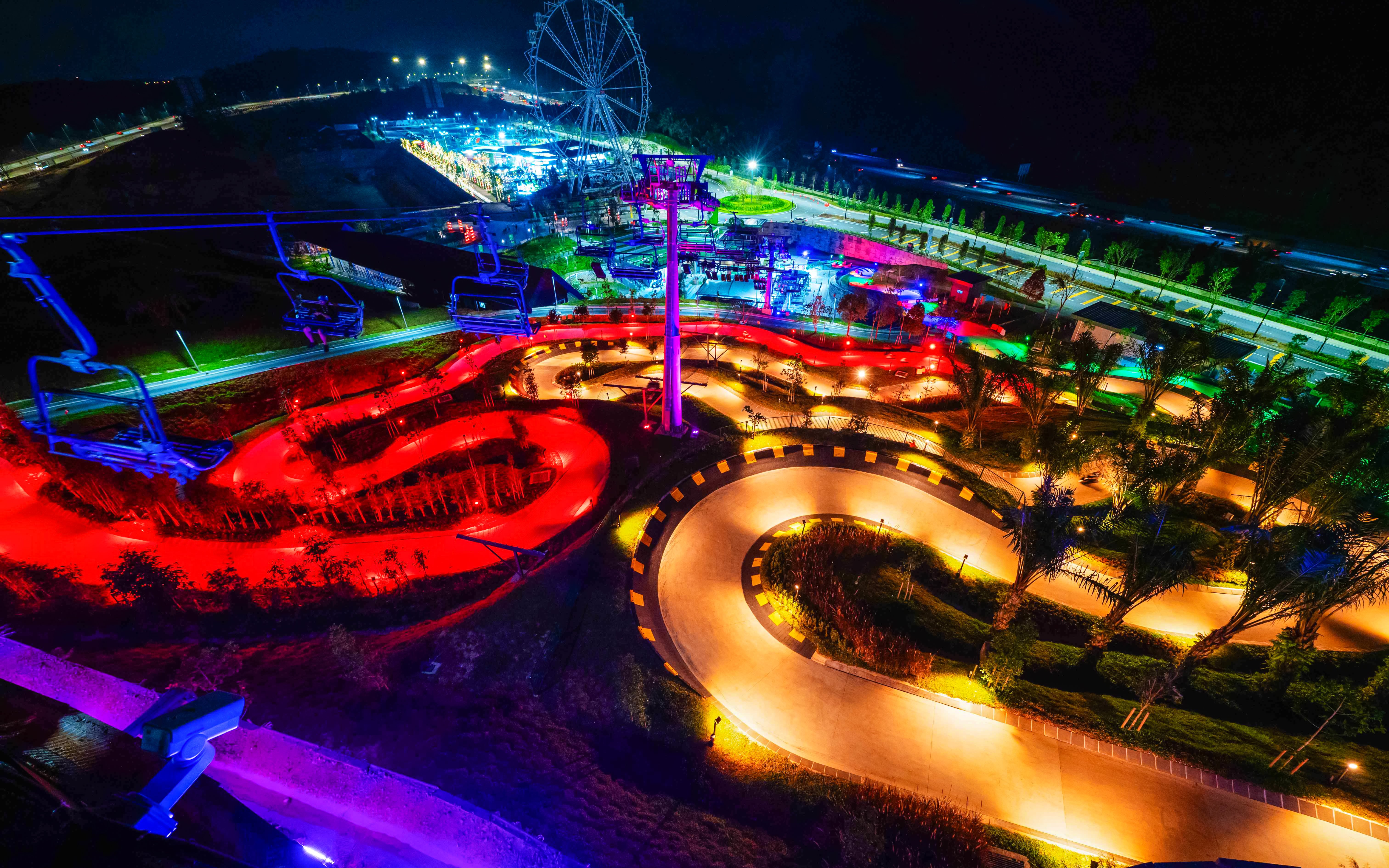 Night view of illuminated tracks and Ferris wheel at Skyline Luge Kuala Lumpur.
