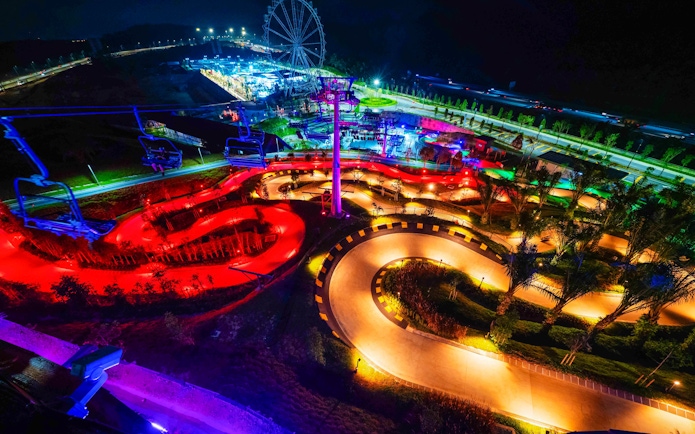 Night view of illuminated tracks and Ferris wheel at Skyline Luge Kuala Lumpur.