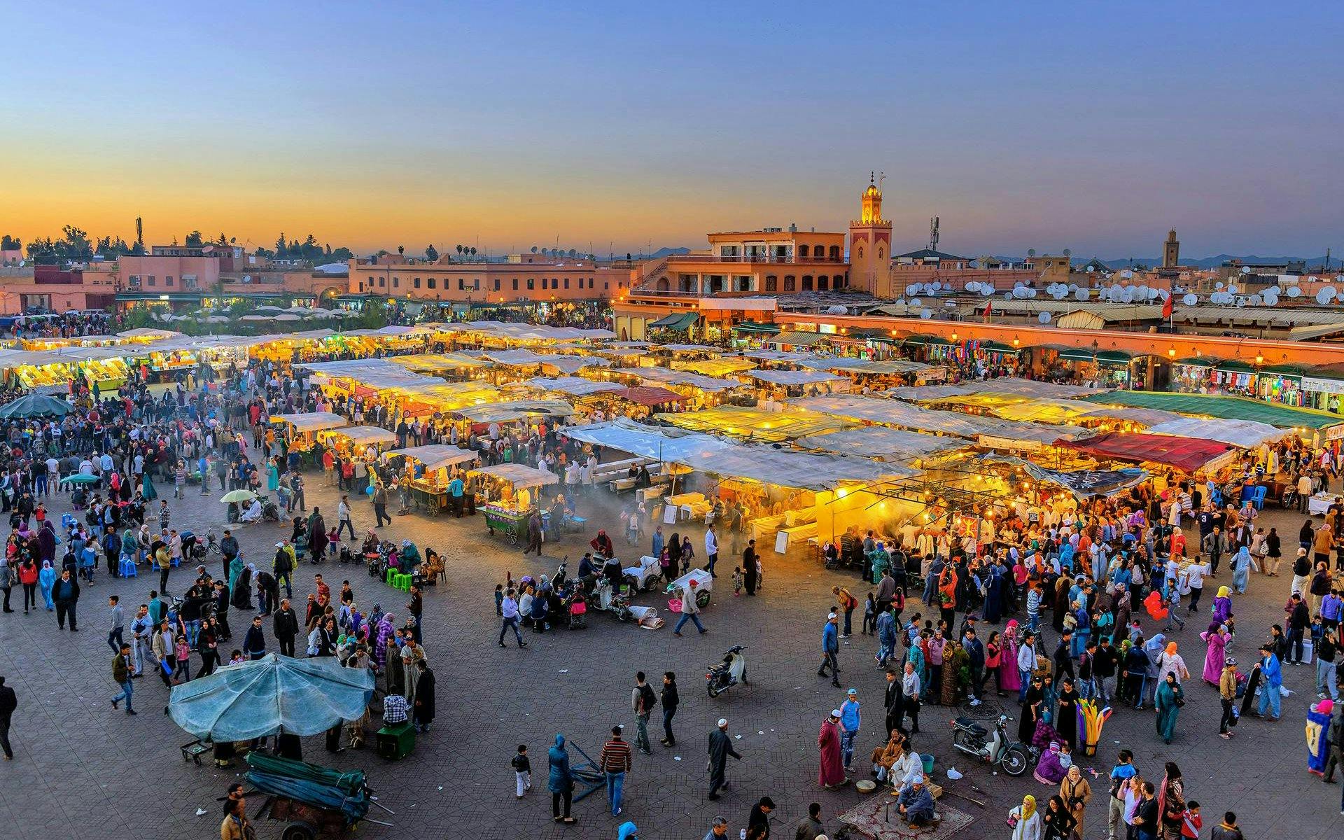 Jemaa el-Fnaa square bustling with people and market stalls at sunset in Marrakech, Morocco.