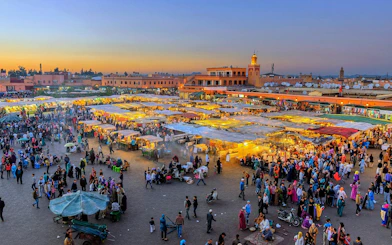 Jemaa el-Fnaa square bustling with people and market stalls at sunset in Marrakech, Morocco.