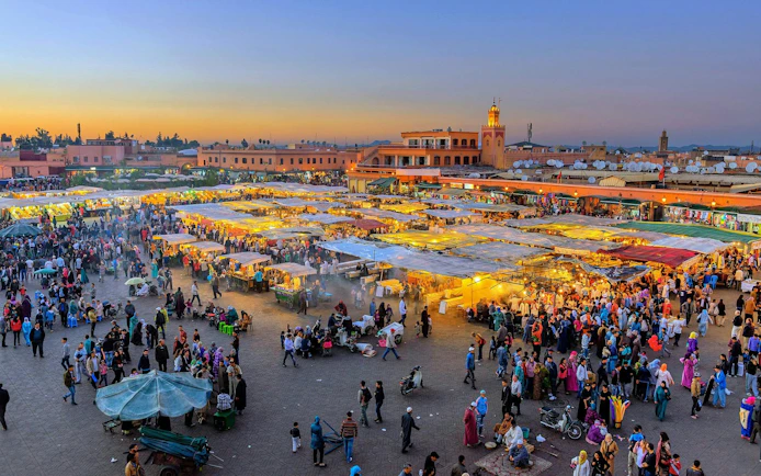 Jemaa el-Fnaa square bustling with people and market stalls at sunset in Marrakech, Morocco.
