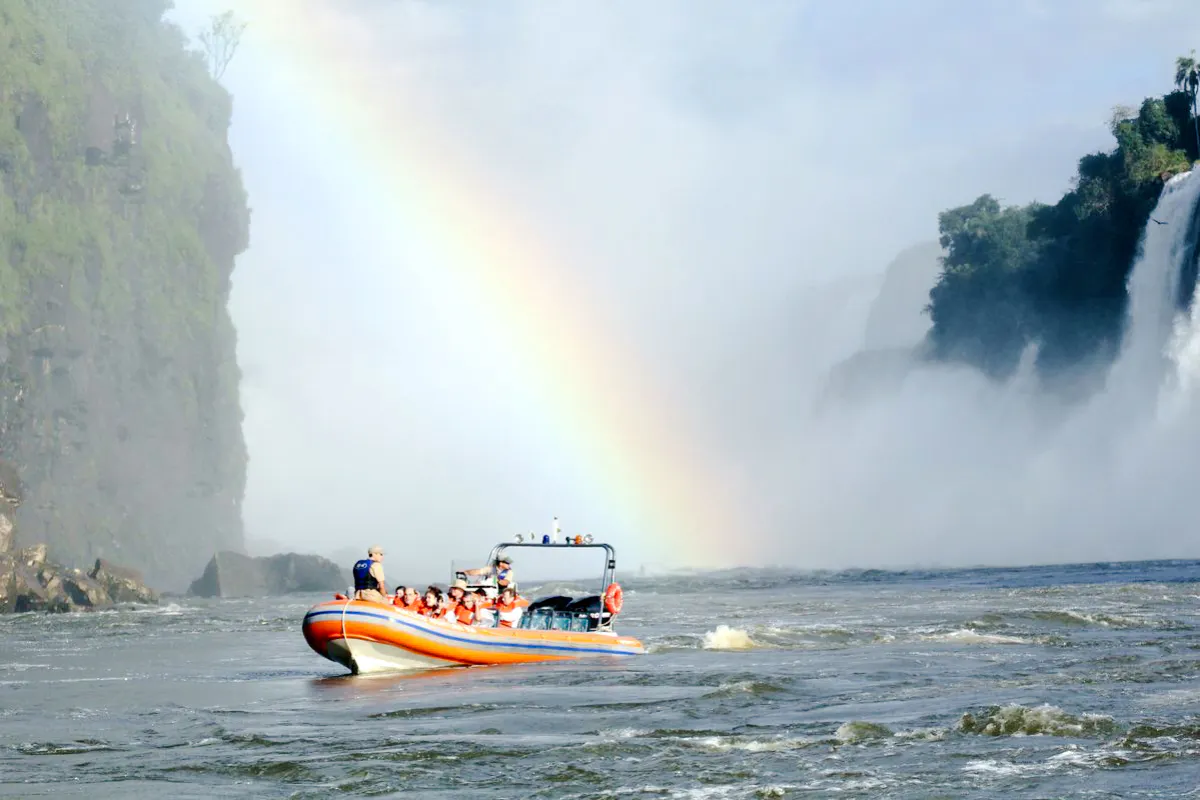 Boat tour approaching Iguazu Falls with rainbow, part of Macuco Safari in Foz do Iguacu.