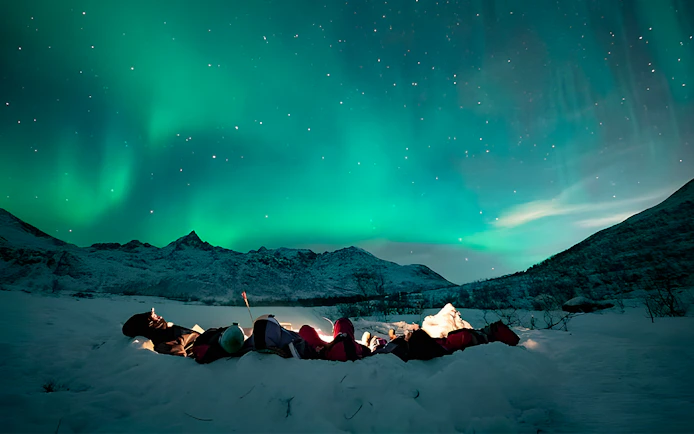 People lying on snow in Tromso watching Northern Lights display.