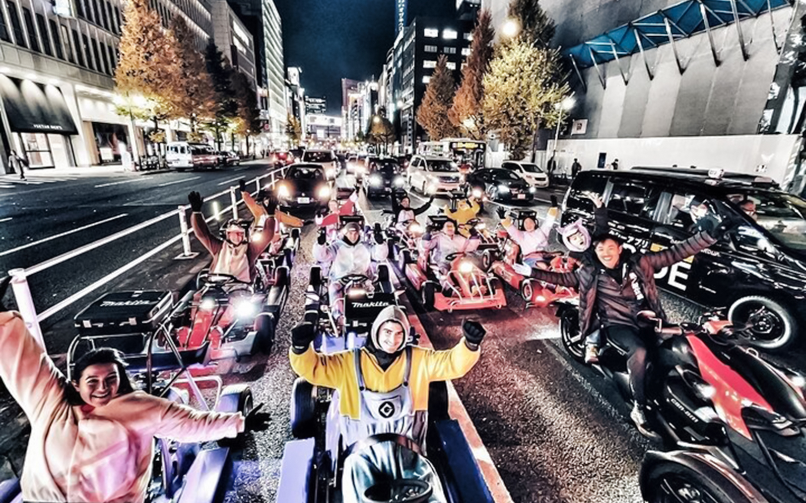 Group in costumes on go-karts driving through a city street at night.