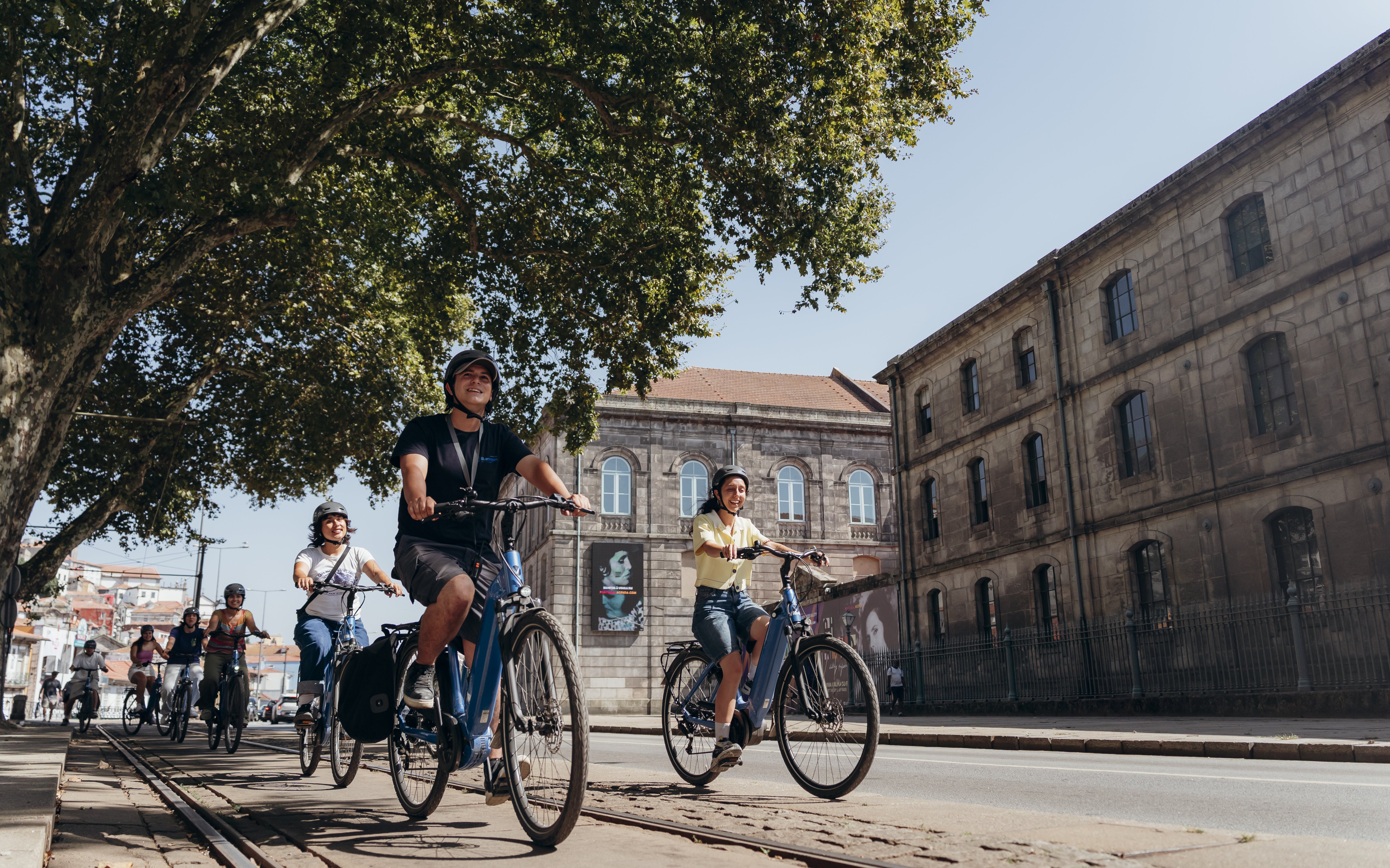 Tourists riding electric bikes with a guide in Porto, passing historic buildings.