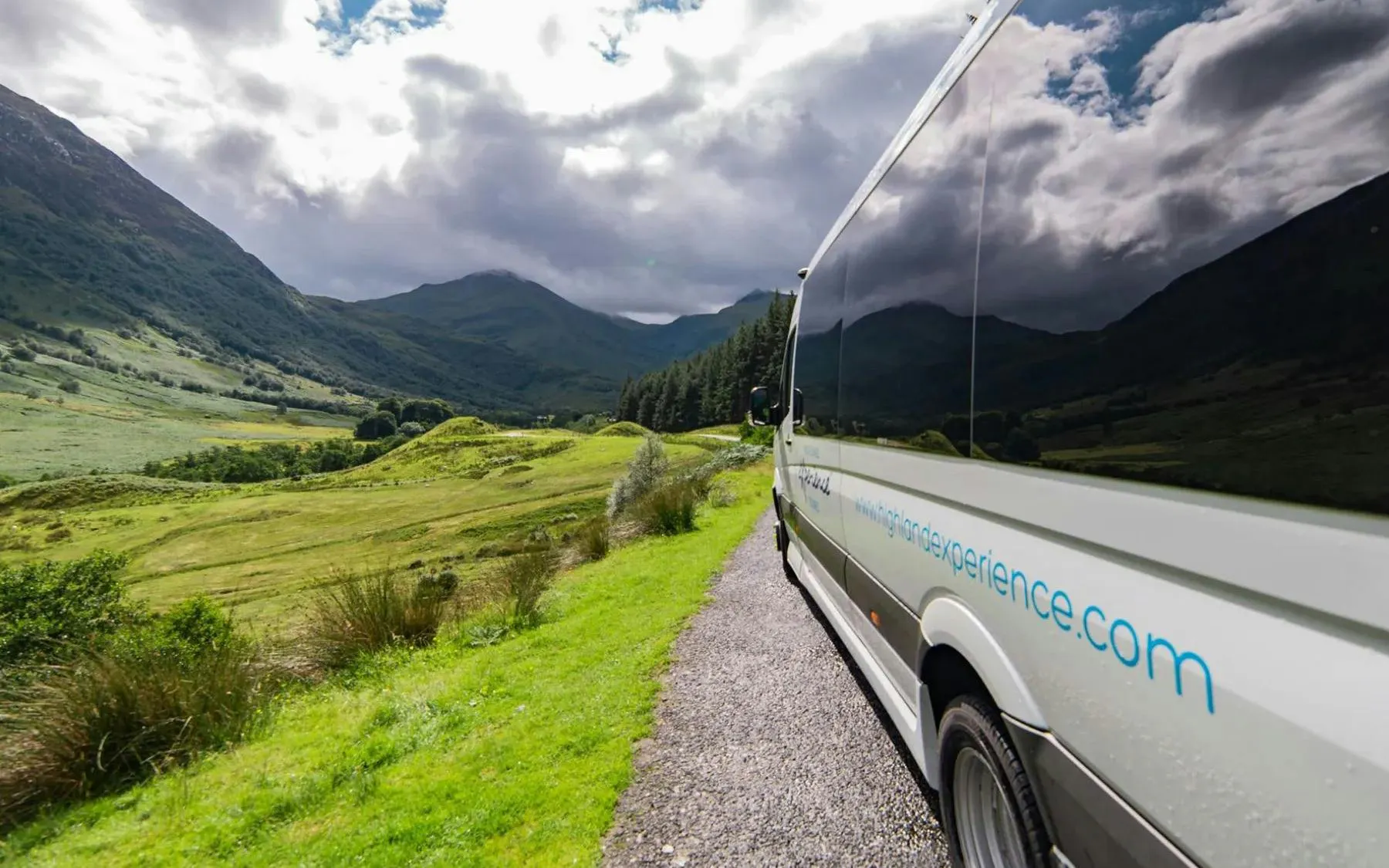 Transfer bus traveling through scenic Scottish Highlands.