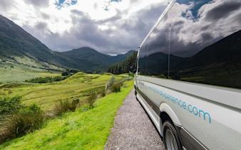 Transfer bus traveling through scenic Scottish Highlands.