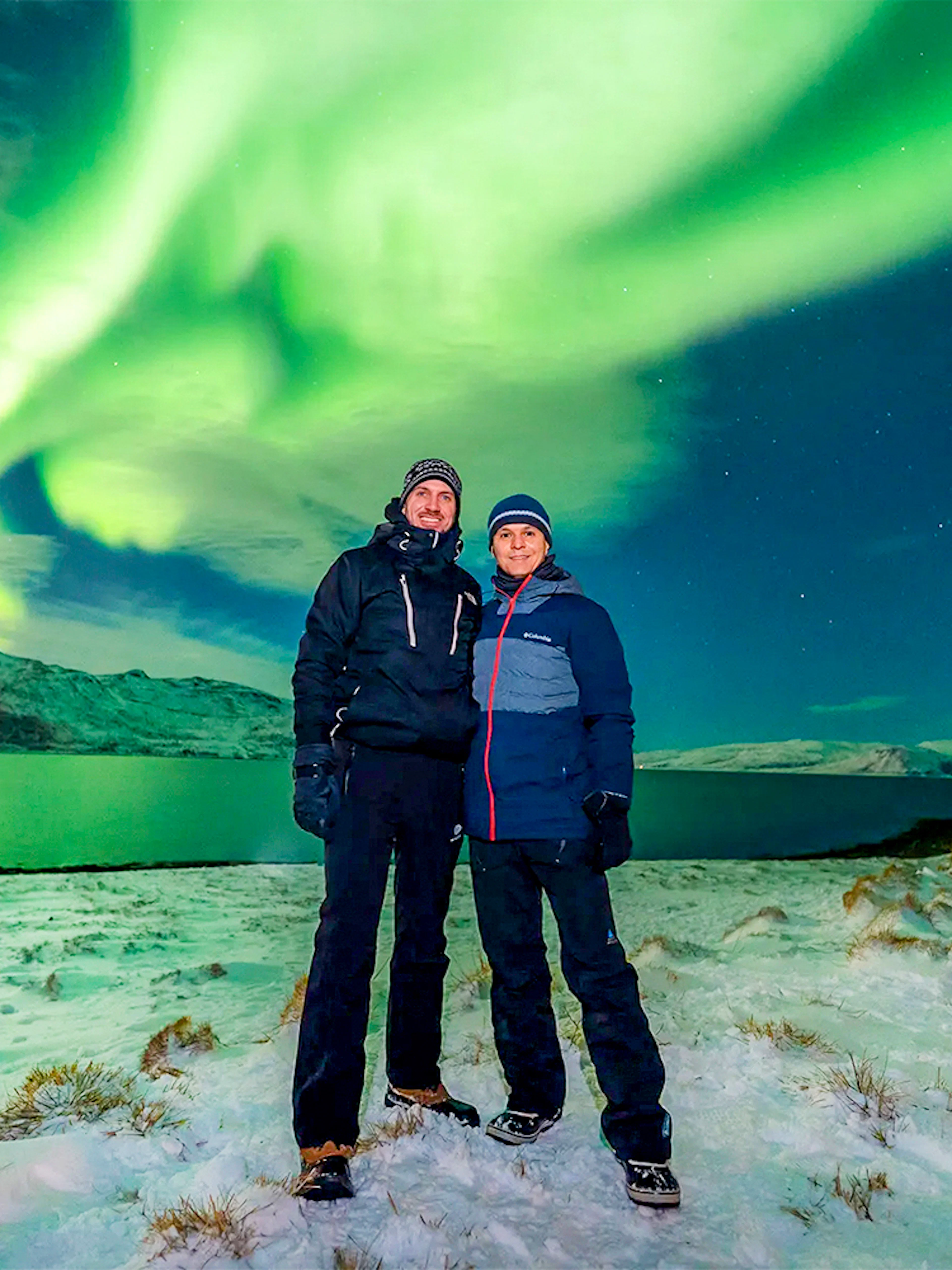 Guests posing under Northern Lights during a tour in a snowy landscape.