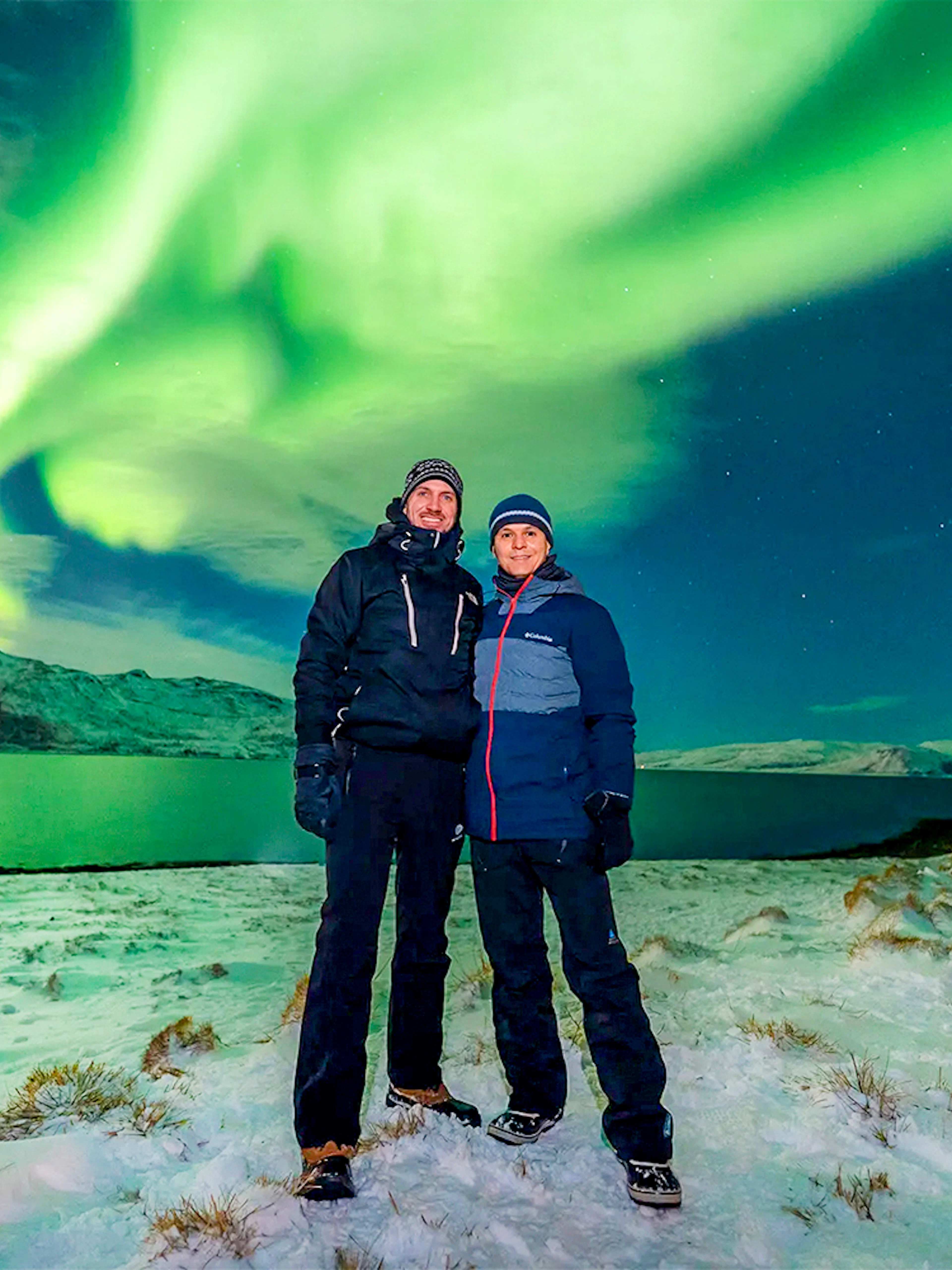 Guests posing under Northern Lights during a tour in a snowy landscape.