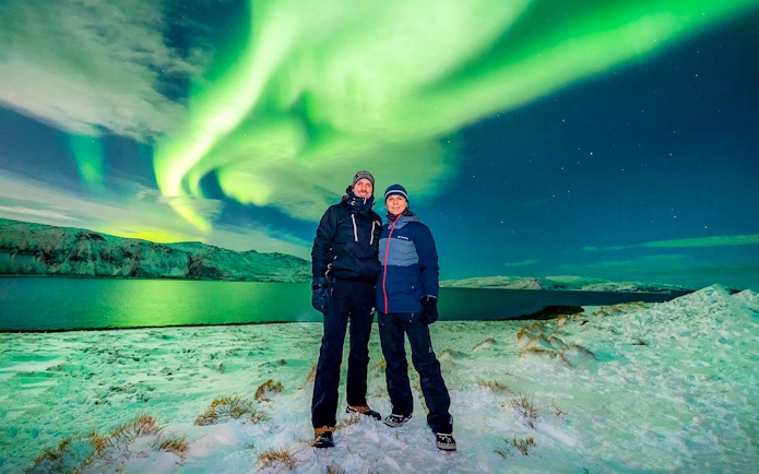 Guests posing under Northern Lights during a tour in a snowy landscape.