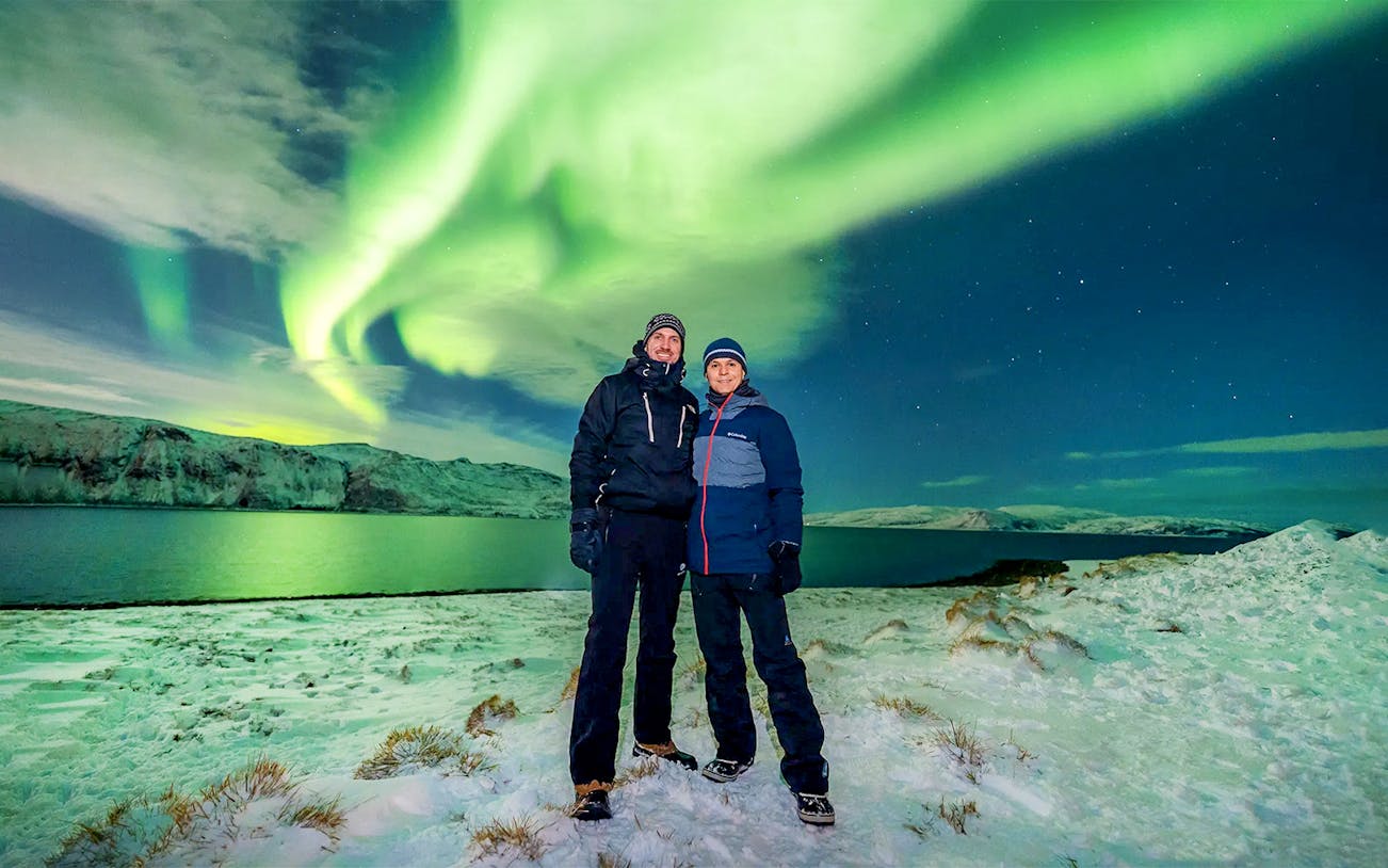 Guests posing under Northern Lights during a tour in a snowy landscape.