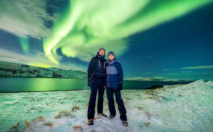 Guests posing under Northern Lights during a tour in a snowy landscape.