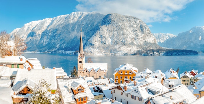 Hallstatt village covered in snow with a church spire and lake, surrounded by winter mountains, Austria.