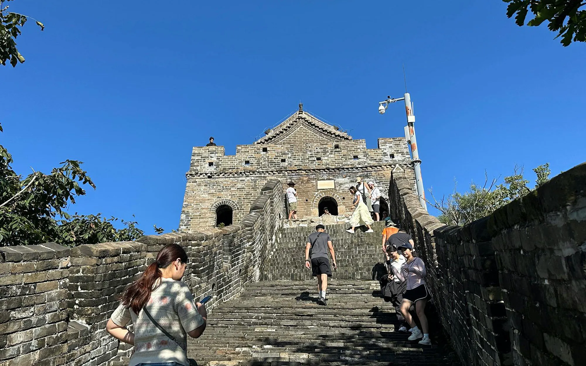 Visitors climbing steps at Mutianyu Great Wall, Beijing, with watchtower in view.