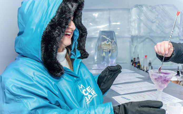 Person enjoying a drink at IceBar Surfers Paradise, wearing a blue parka.