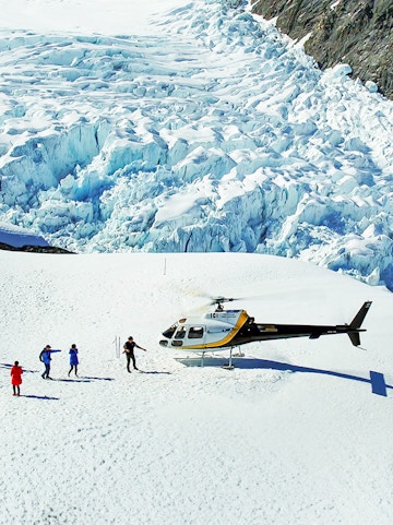 Helicopter landing on Franz Josef Glacier with hikers nearby.