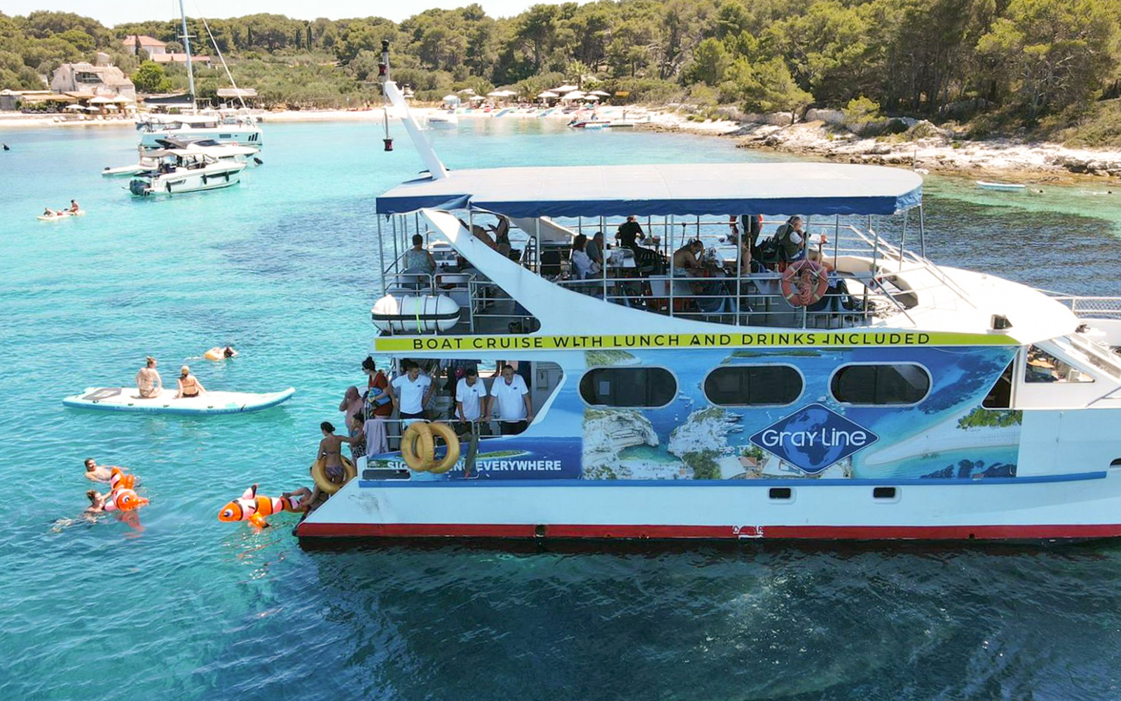 Boat cruise near Trogir with people swimming and paddleboarding in clear water.