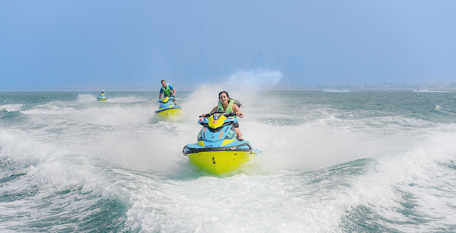 Jet ski rider navigating waves with Dubai skyline in the background.