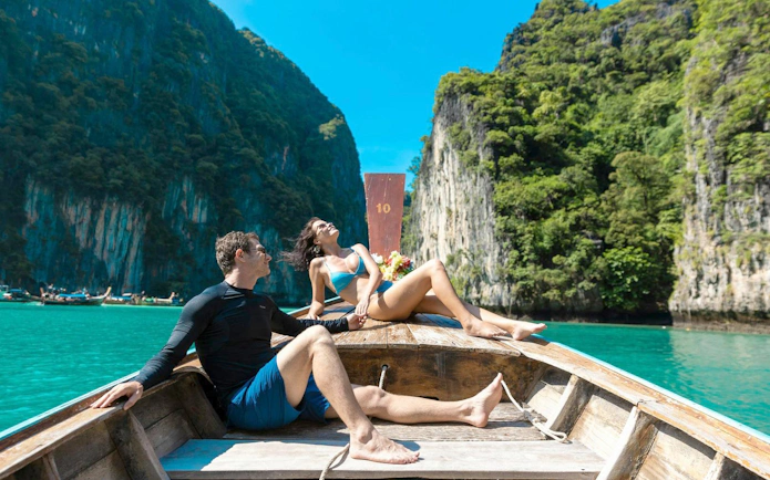 Couple relaxing on a boat in turquoise waters near limestone cliffs, Phi Phi Islands tour, Phuket.
