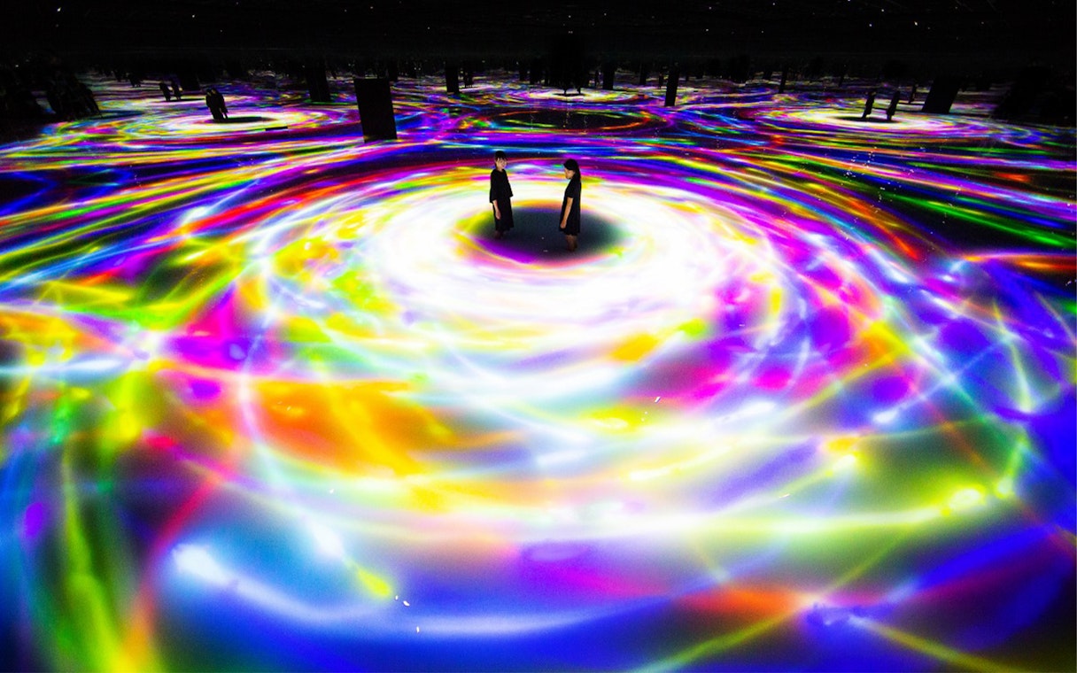 Visitors at TeamLab Planets Tokyo surrounded by swirling colorful digital light displays.