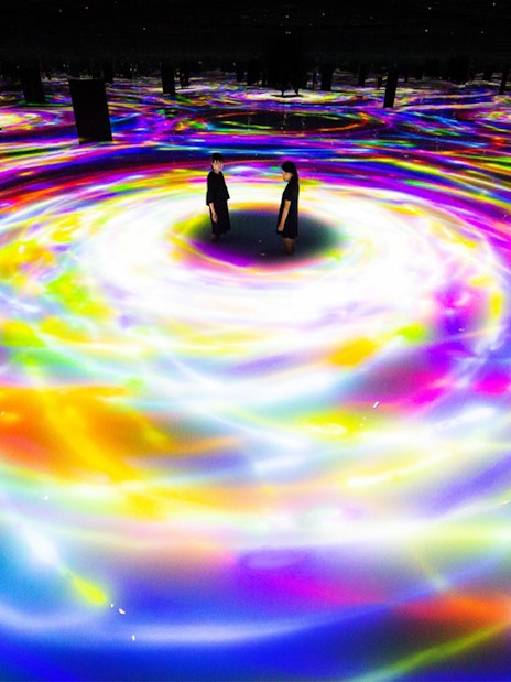 Visitors at TeamLab Planets Tokyo surrounded by swirling colorful digital light displays.