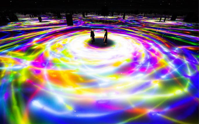 Visitors at TeamLab Planets Tokyo surrounded by swirling colorful digital light displays.