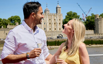 Guests enjoying drinks on a Tower of London cruise with the historic castle in the background.
