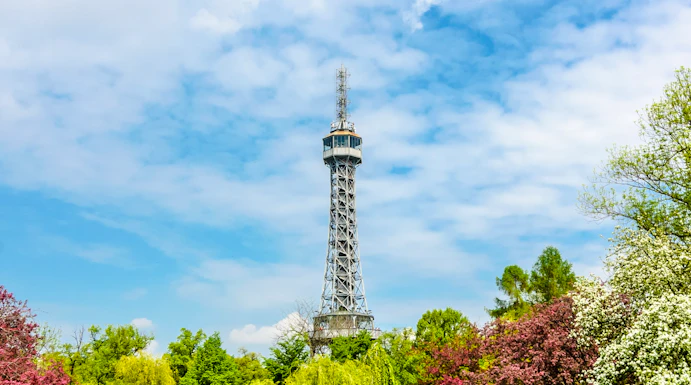 Petrin Tower in Prague surrounded by lush gardens and colorful trees.