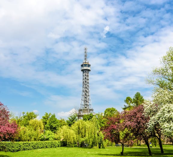 Petrin Tower in Prague surrounded by lush gardens and colorful trees.