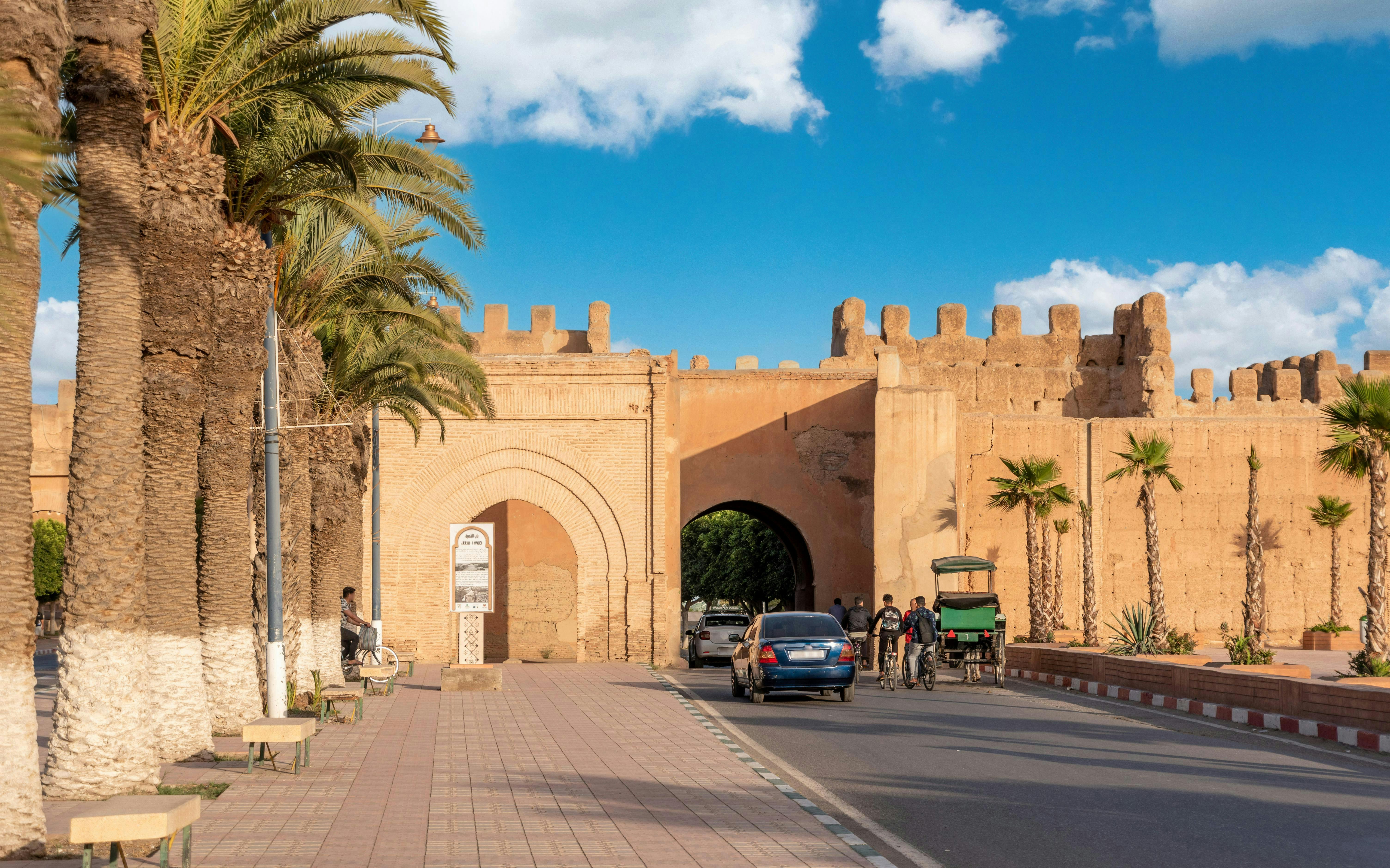 Bab Selsla gate at Taroudannt city walls, Morocco, with palm trees and people passing by.