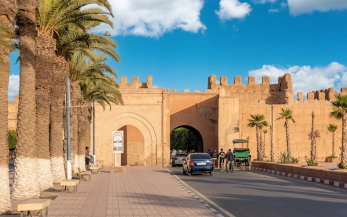 Bab Selsla gate at Taroudannt city walls, Morocco, with palm trees and people passing by.
