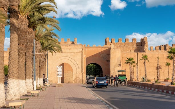 Bab Selsla gate at Taroudannt city walls, Morocco, with palm trees and people passing by.