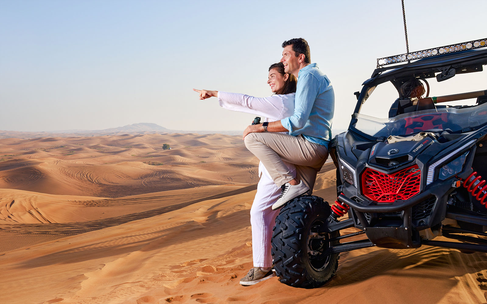 Couple sitting on a buggy in Noble Camp Desert Safari, pointing at sand dunes.