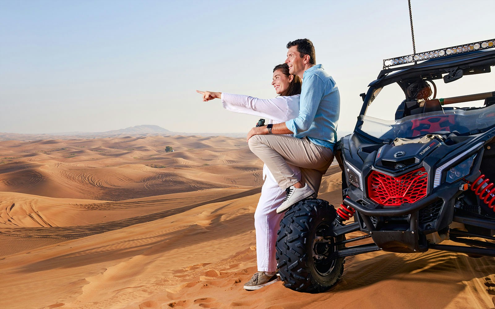 Couple sitting on a buggy in Noble Camp Desert Safari, pointing at sand dunes.