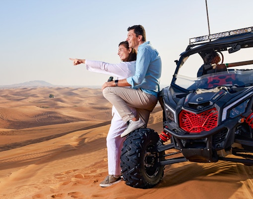 Couple sitting on a buggy in Noble Camp Desert Safari, pointing at sand dunes.
