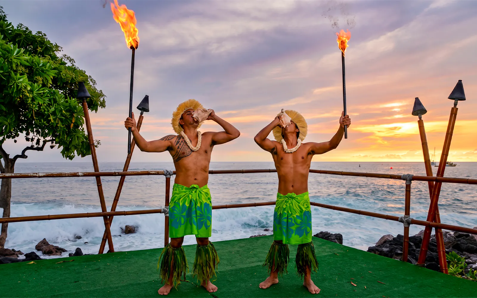 Performers blowing conch shells at sunset during Voyagers of the Pacific Luau in Hawaii.
