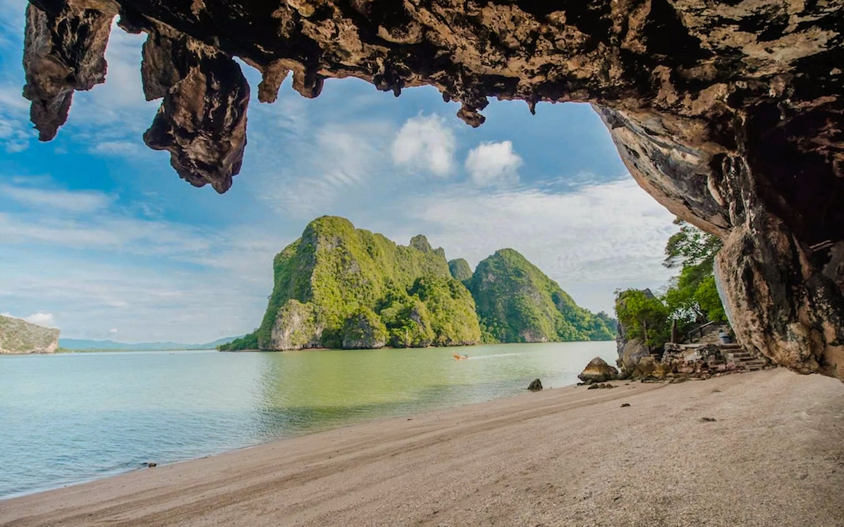 Limestone formations and clear emerald water at a beach with distant green hills.
