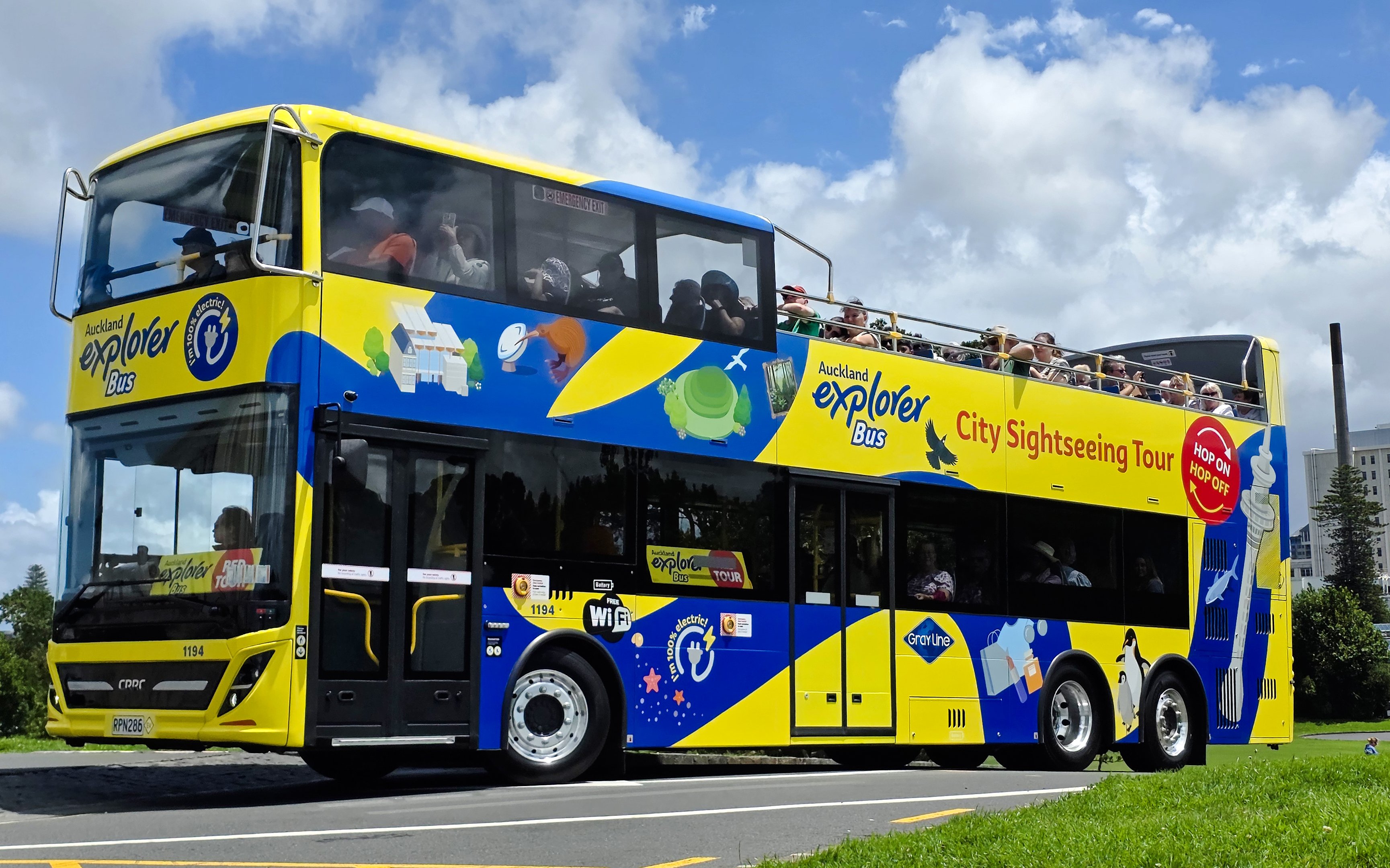 Auckland Explorer Bus on a sunny day with tourists on the upper deck.