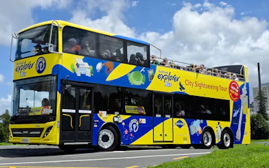 Auckland Explorer Bus on a sunny day with tourists on the upper deck.